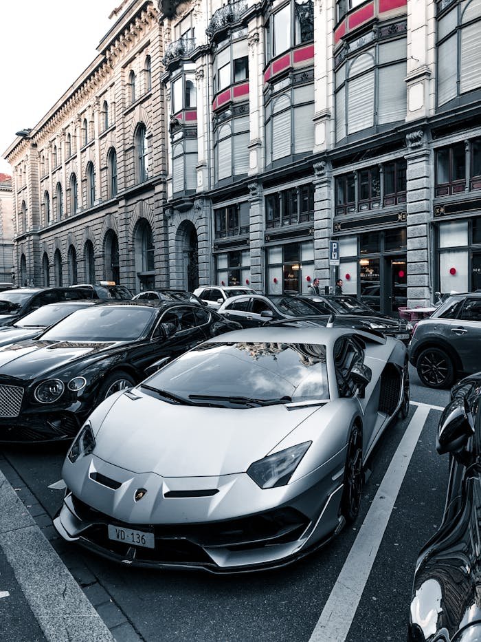 A collection of luxury sports cars, including a Lamborghini, parked on an urban street with classic architecture.