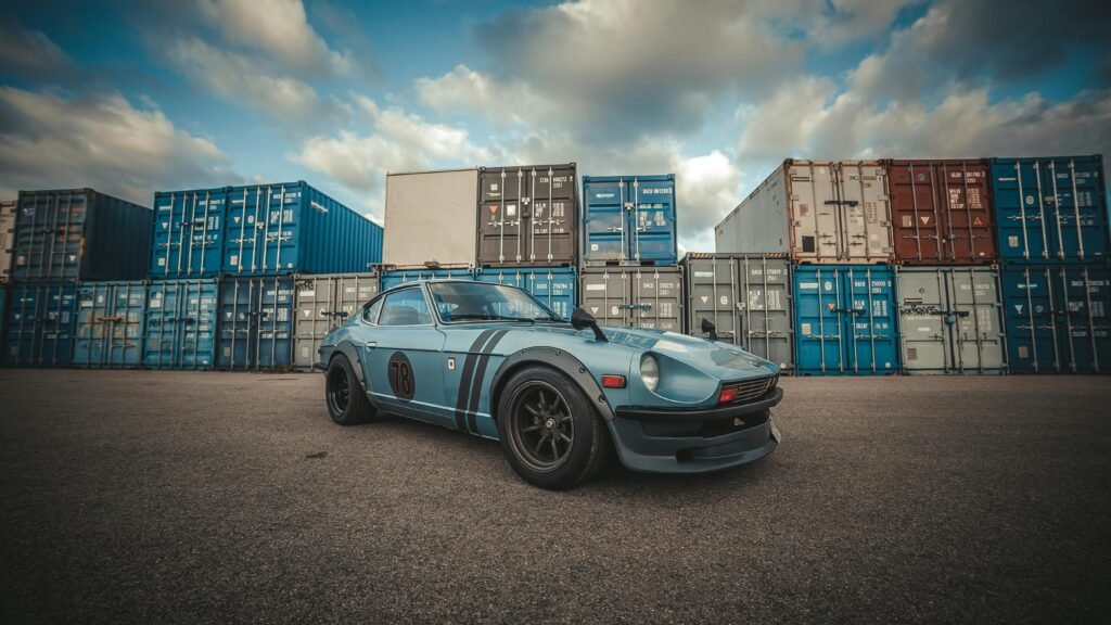 Import Car from USA to UAE A classic Datsun 280Z parked in front of colorful shipping containers under a blue sky.